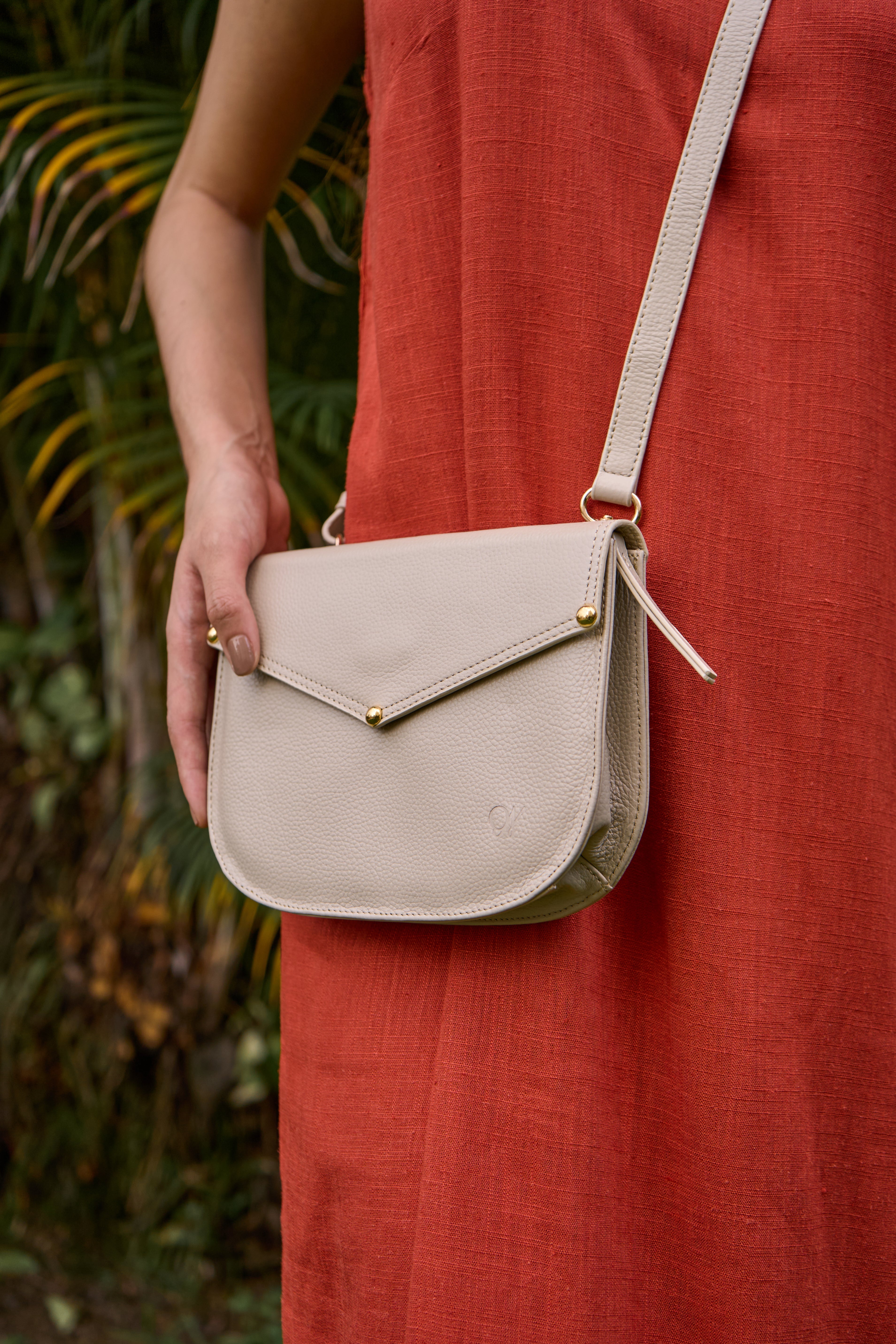 Beige handbag worn by a person in a red dress with a blurred natural background