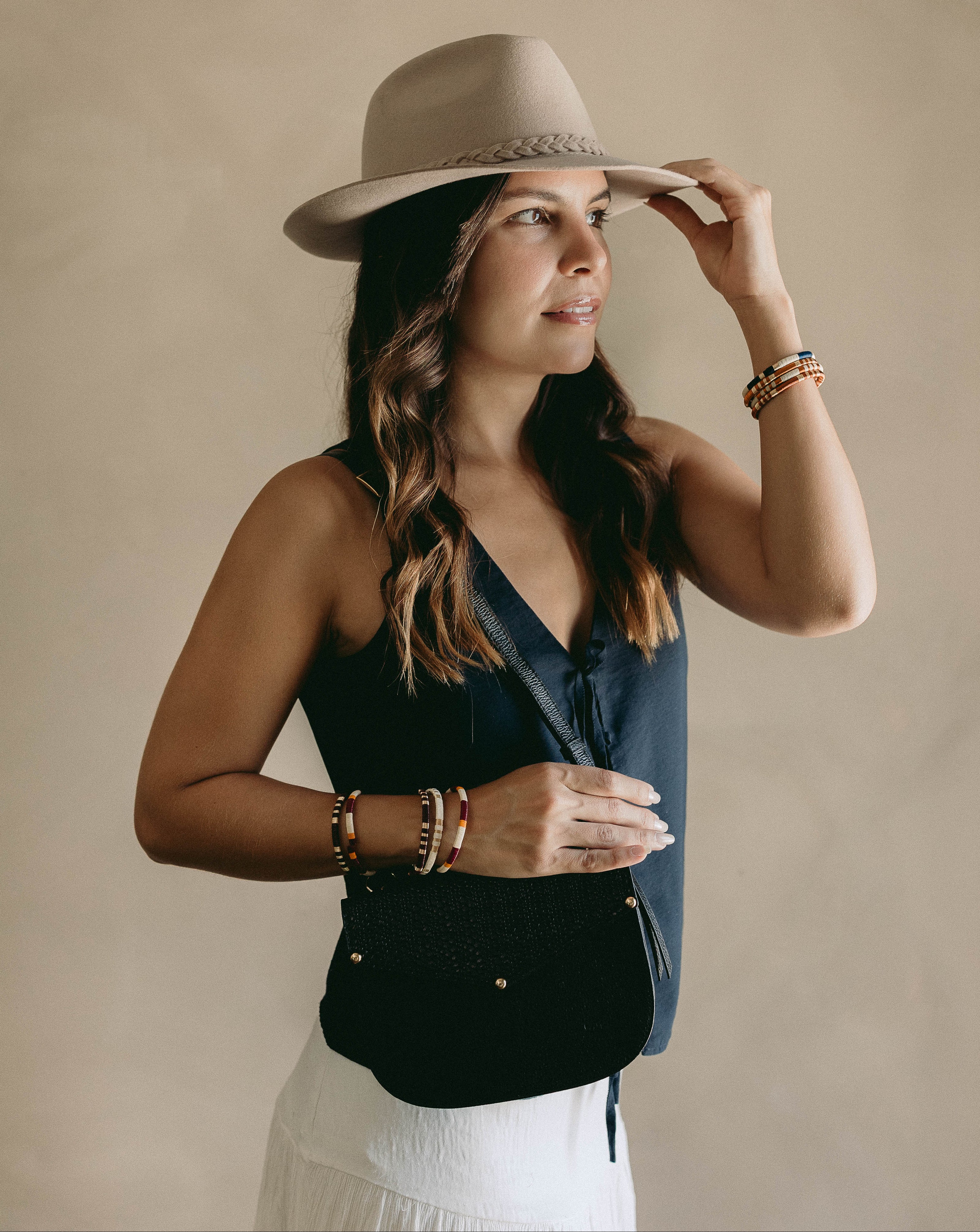 Woman wearing a beige hat and black top against a beige background, with black bag