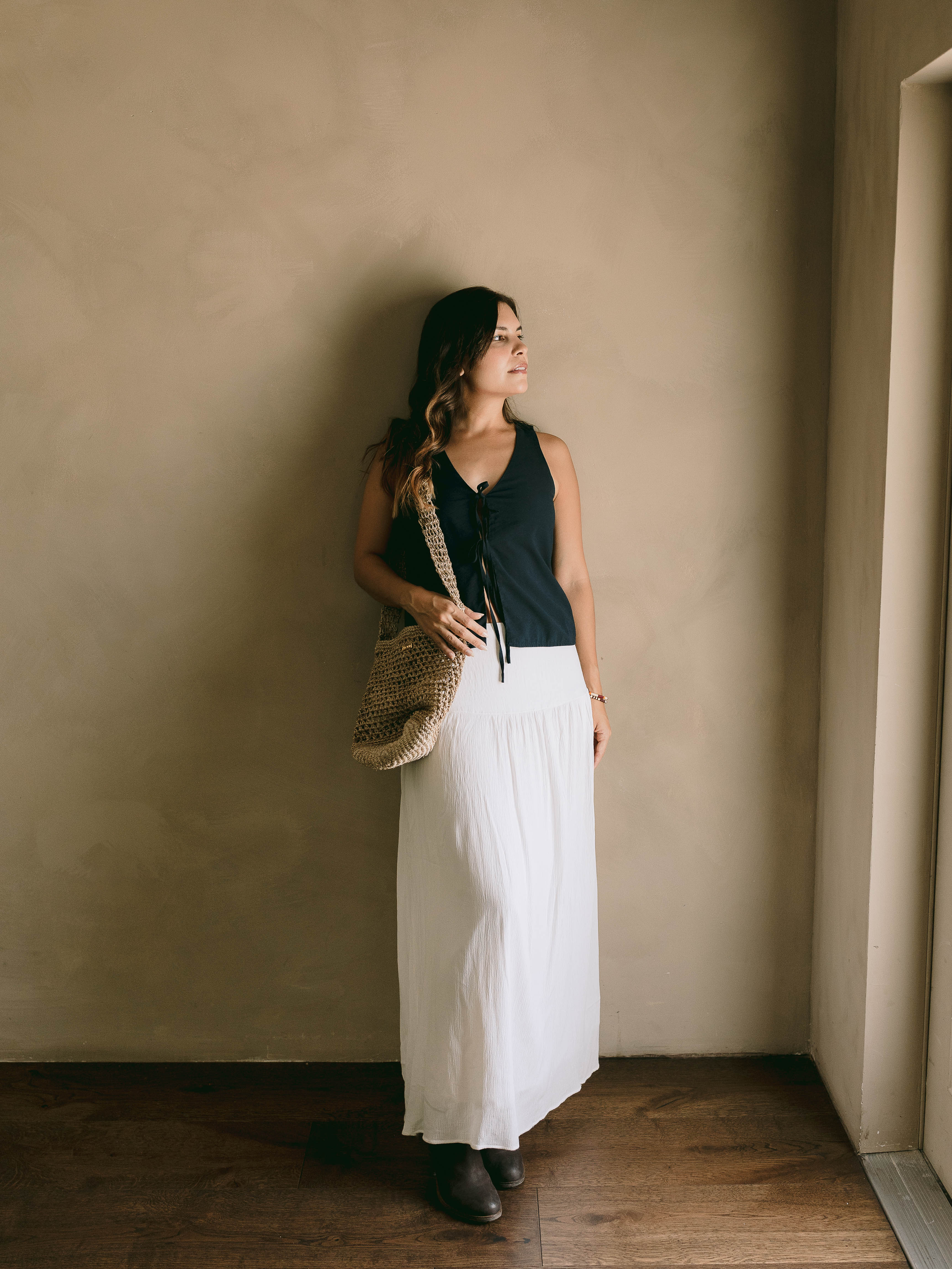 Woman holding a woven bag against a beige wall