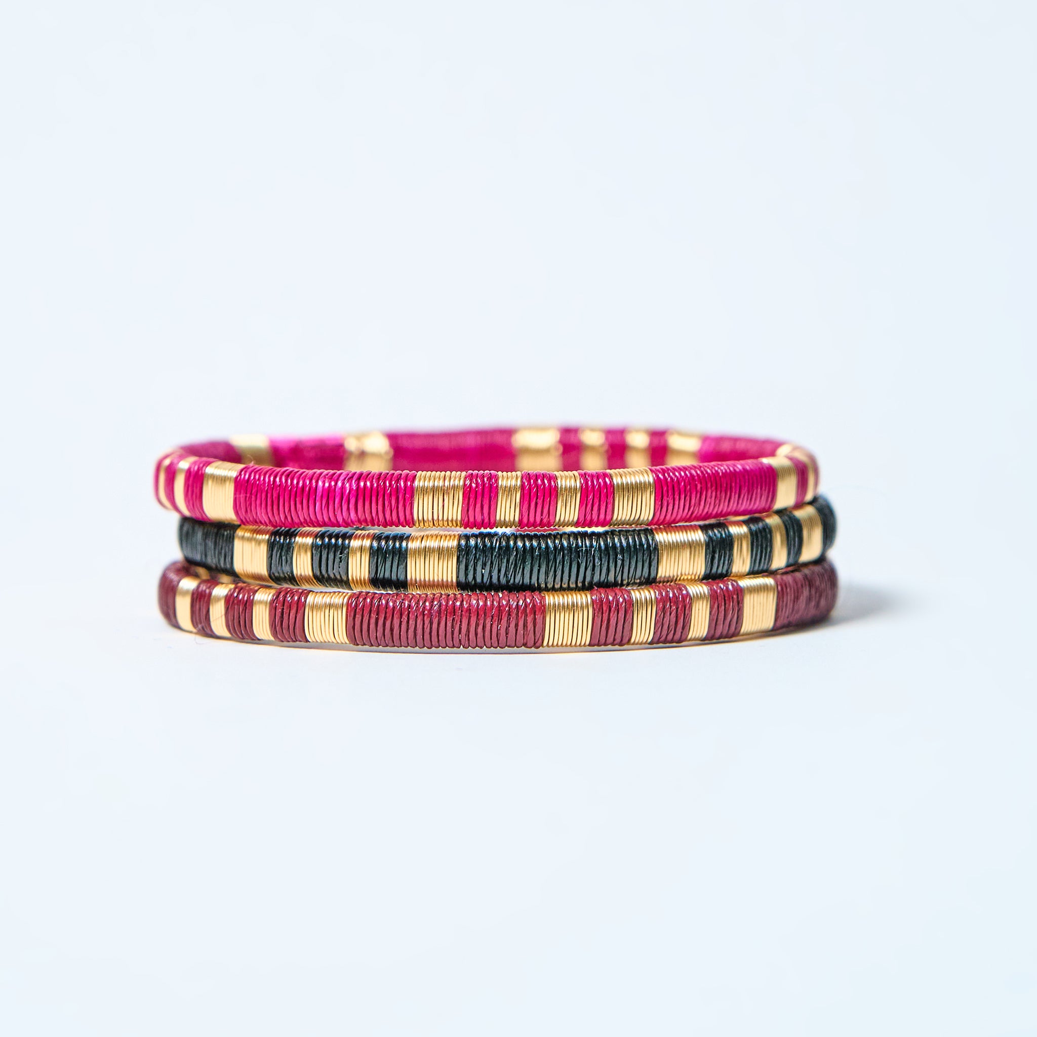 Set of colorful woven bracelets, fuchsia, black, gold, and wine red on a light gray background