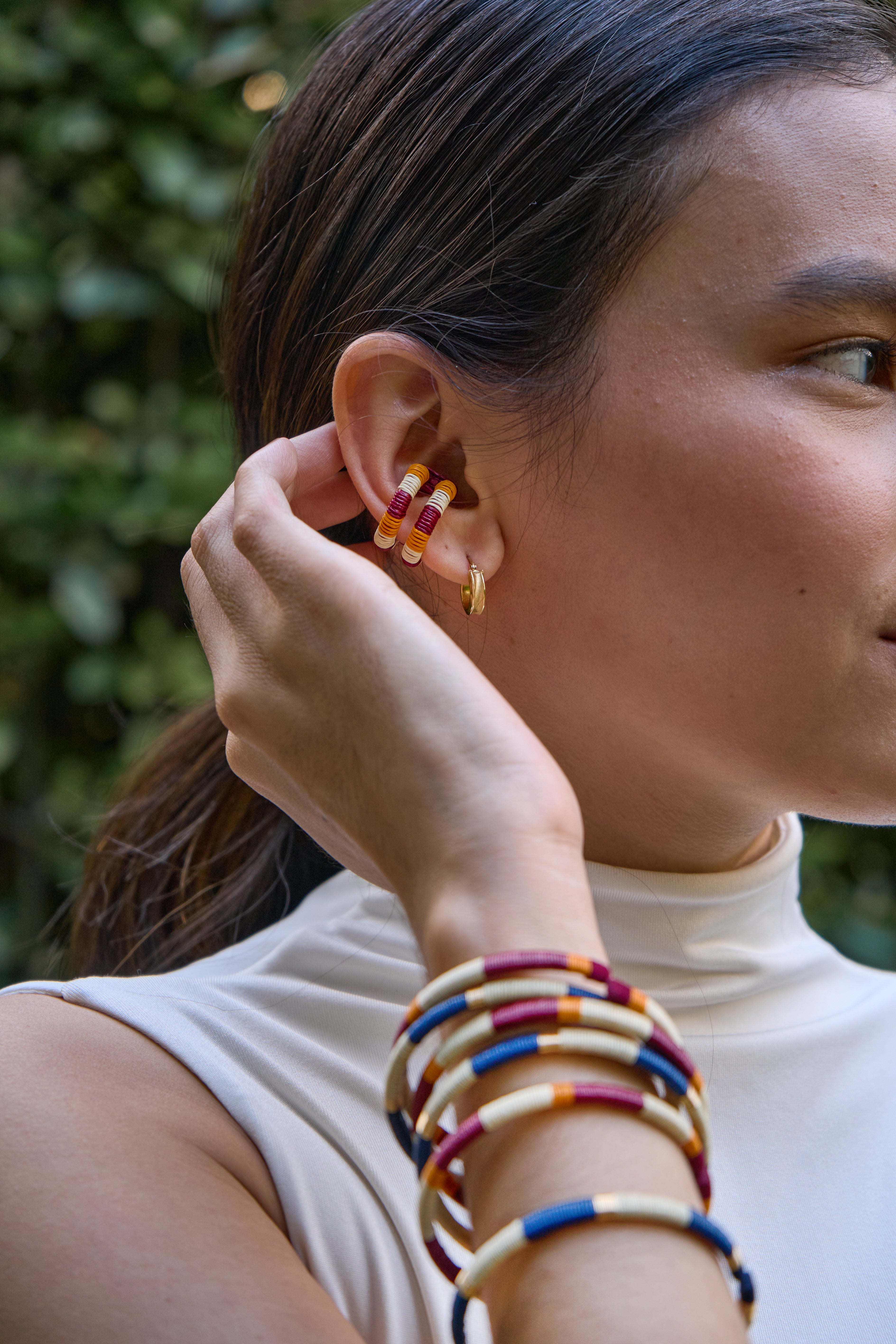 Model wearing colorful ear cuff striped in red wine, mustard and cream. And bracelets