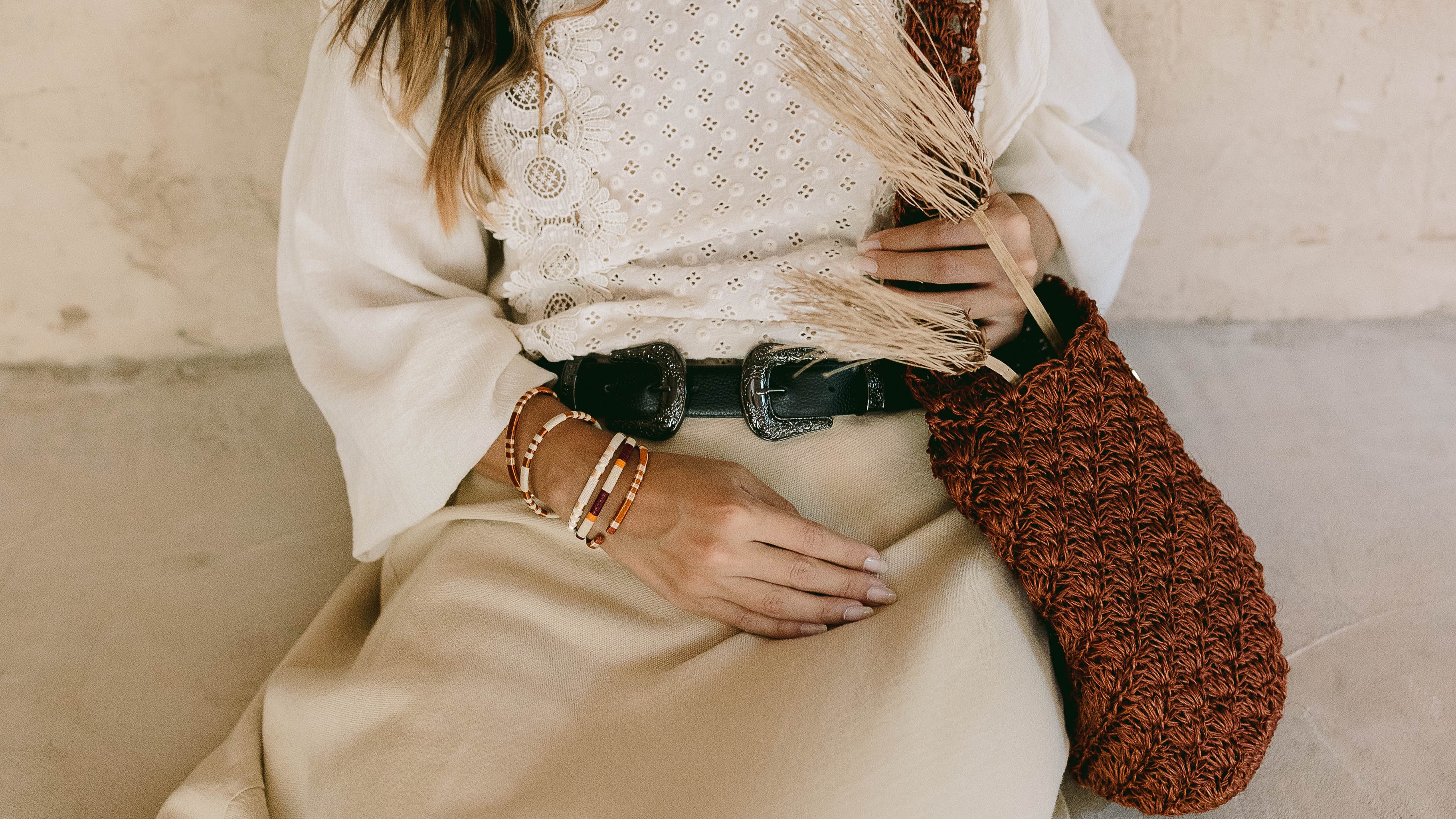 Woman holding a woven bag against a beige wall