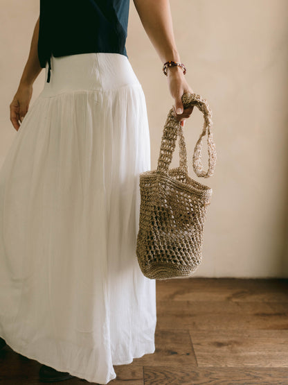 Person holding a woven bag wearing a white skirt and dark top.