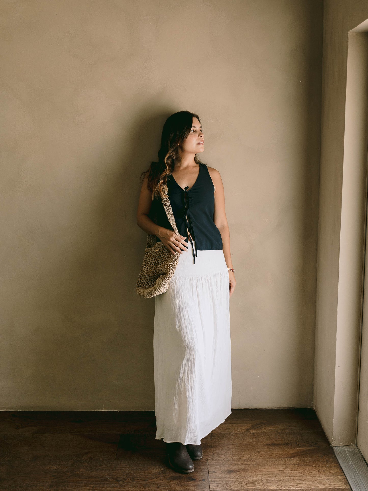 Woman holding a woven bag against a beige wall