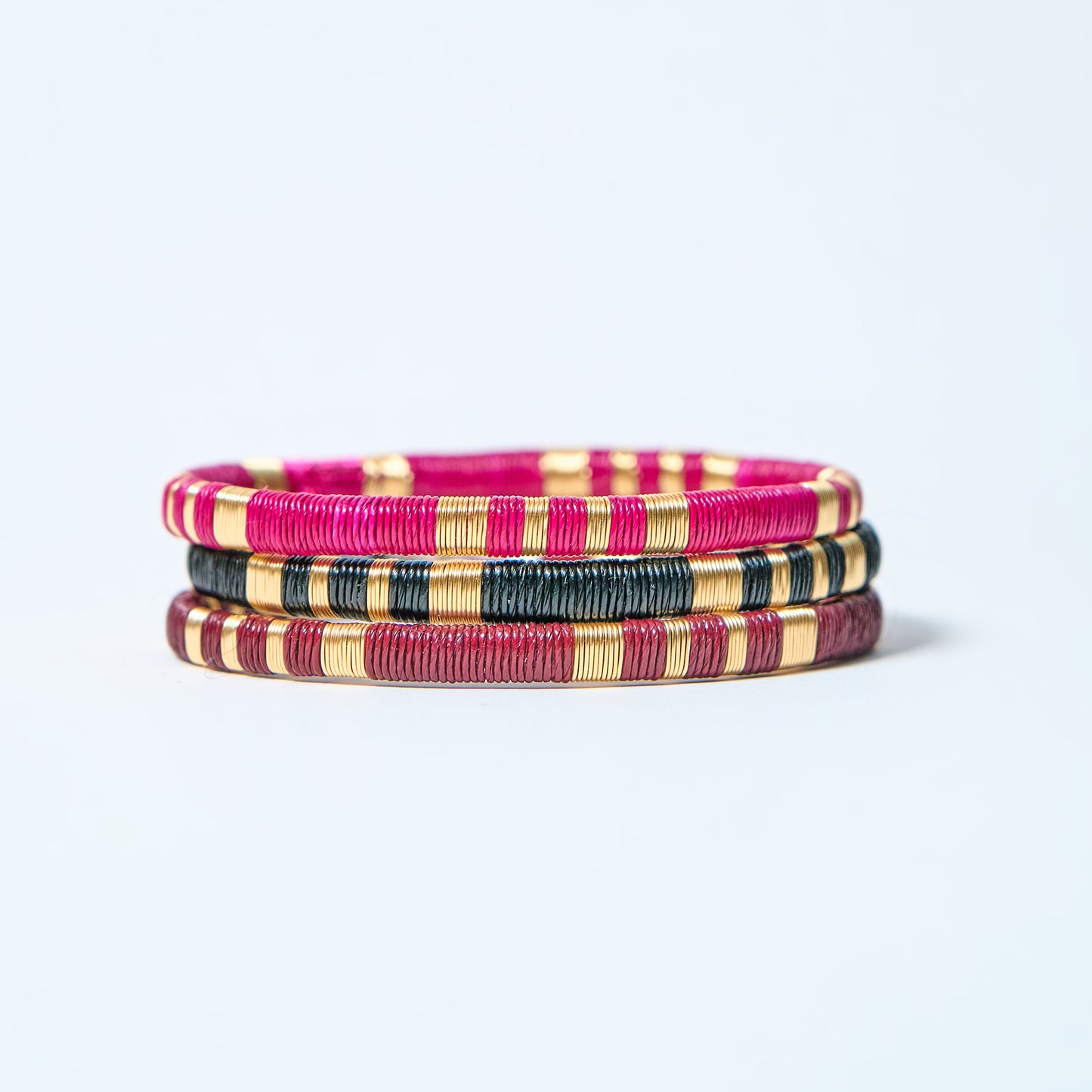 Set of colorful woven bracelets, fuchsia, black, gold, and wine red on a light gray background