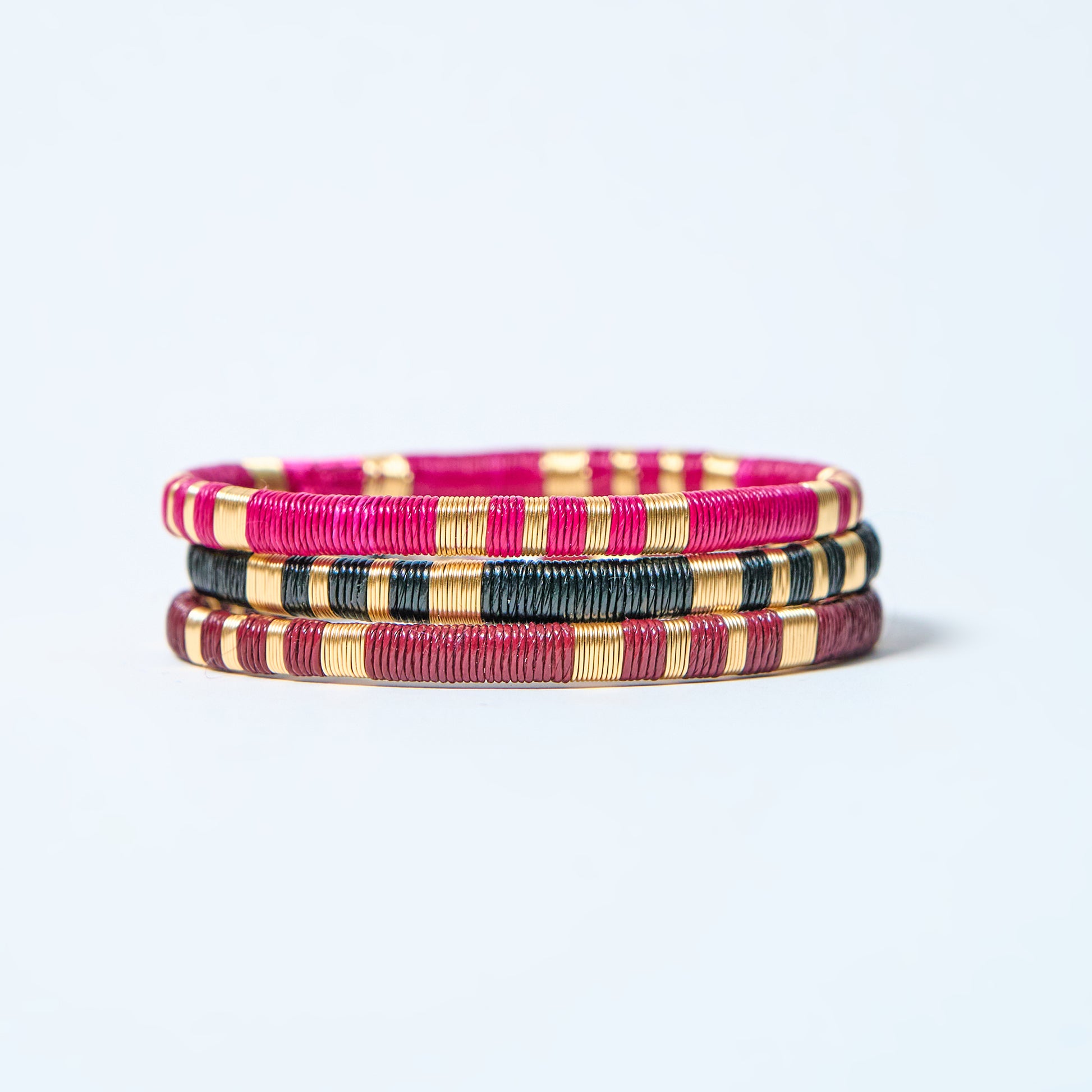 Set of colorful woven bracelets, fuchsia, black, gold, and wine red on a light gray background