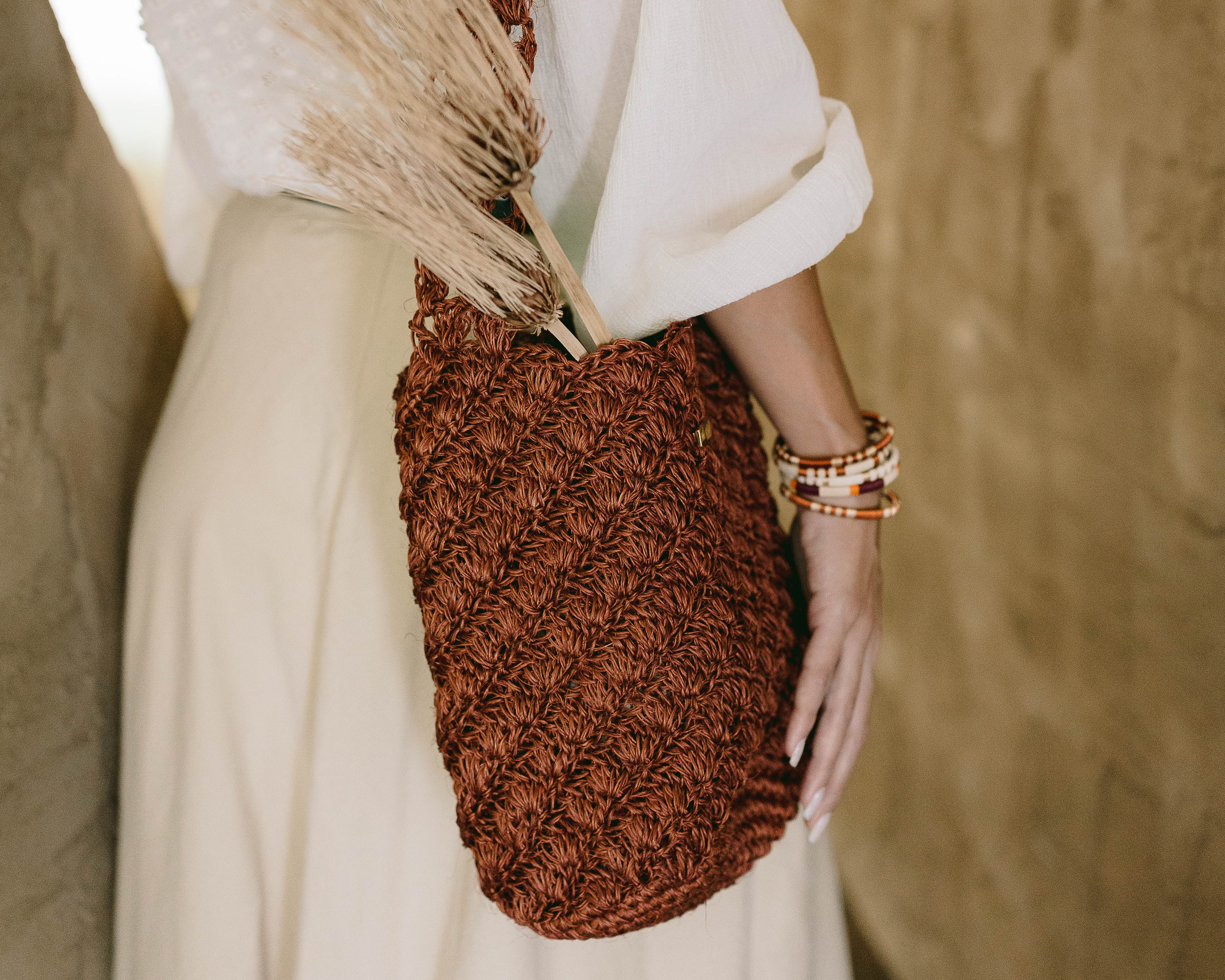 Person holding a brown woven bag with a blurred background