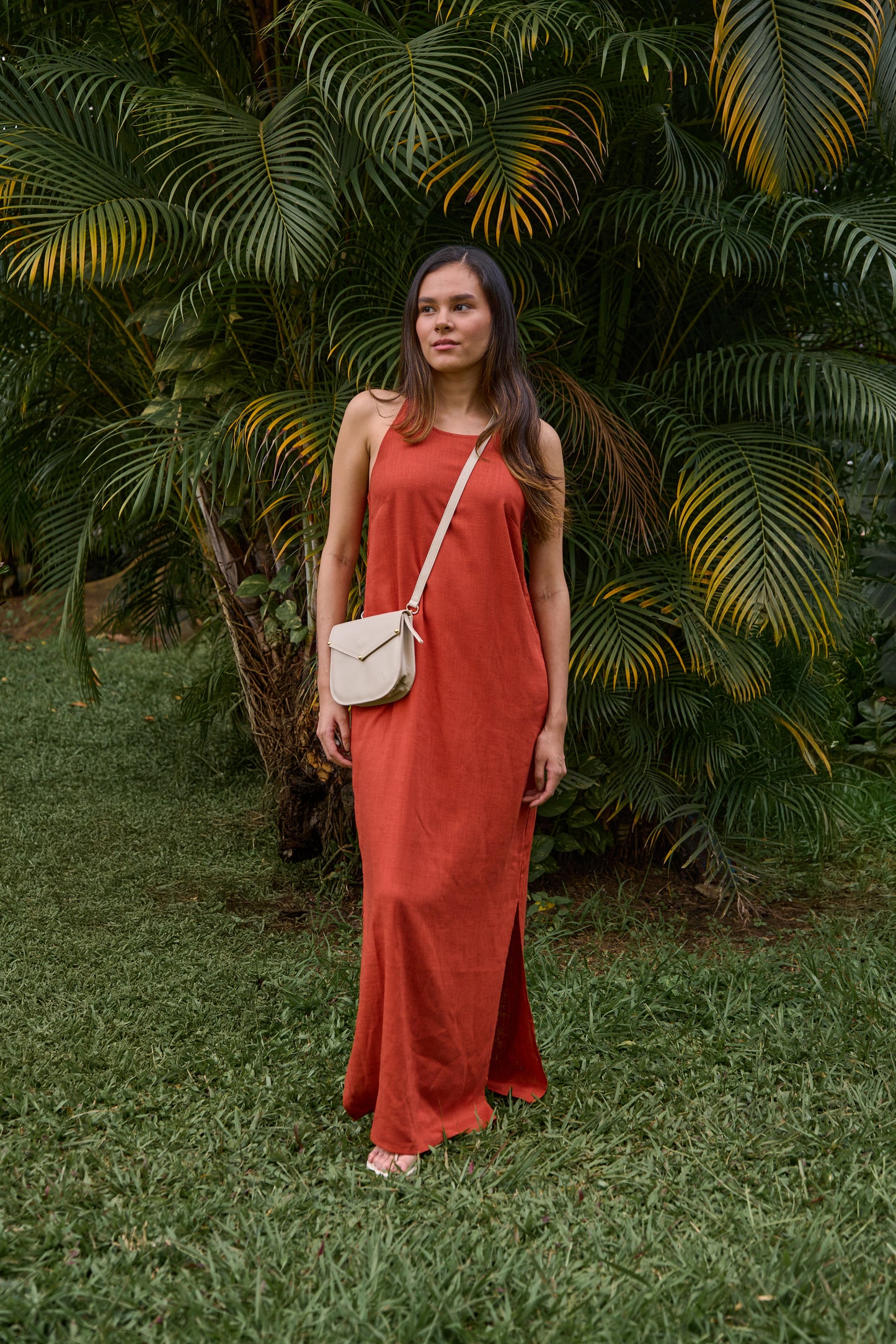 Woman in a red dress standing in a lush green garden with a leather crossbody bag