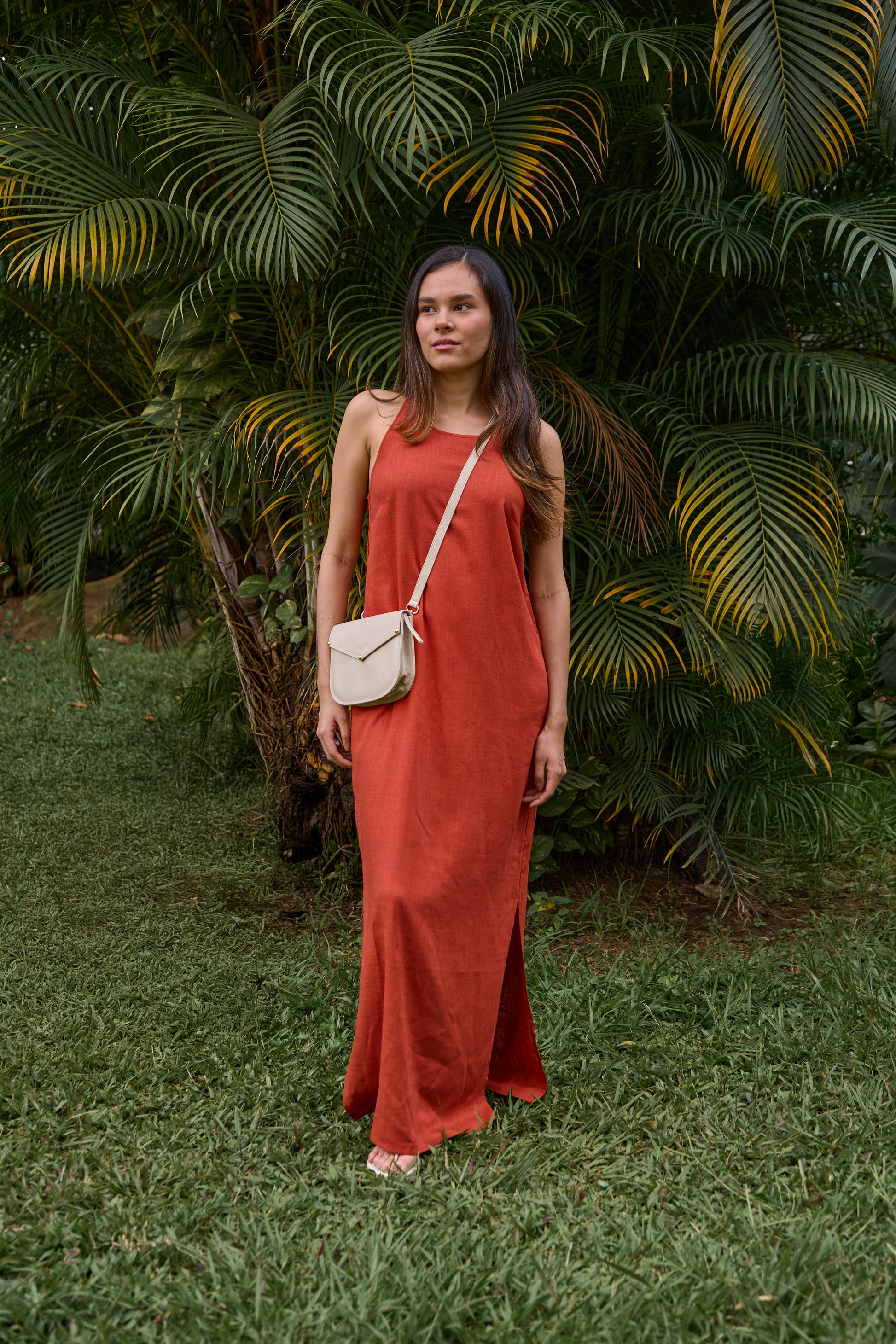 Woman in a red dress standing in a lush green garden with a leather crossbody bag