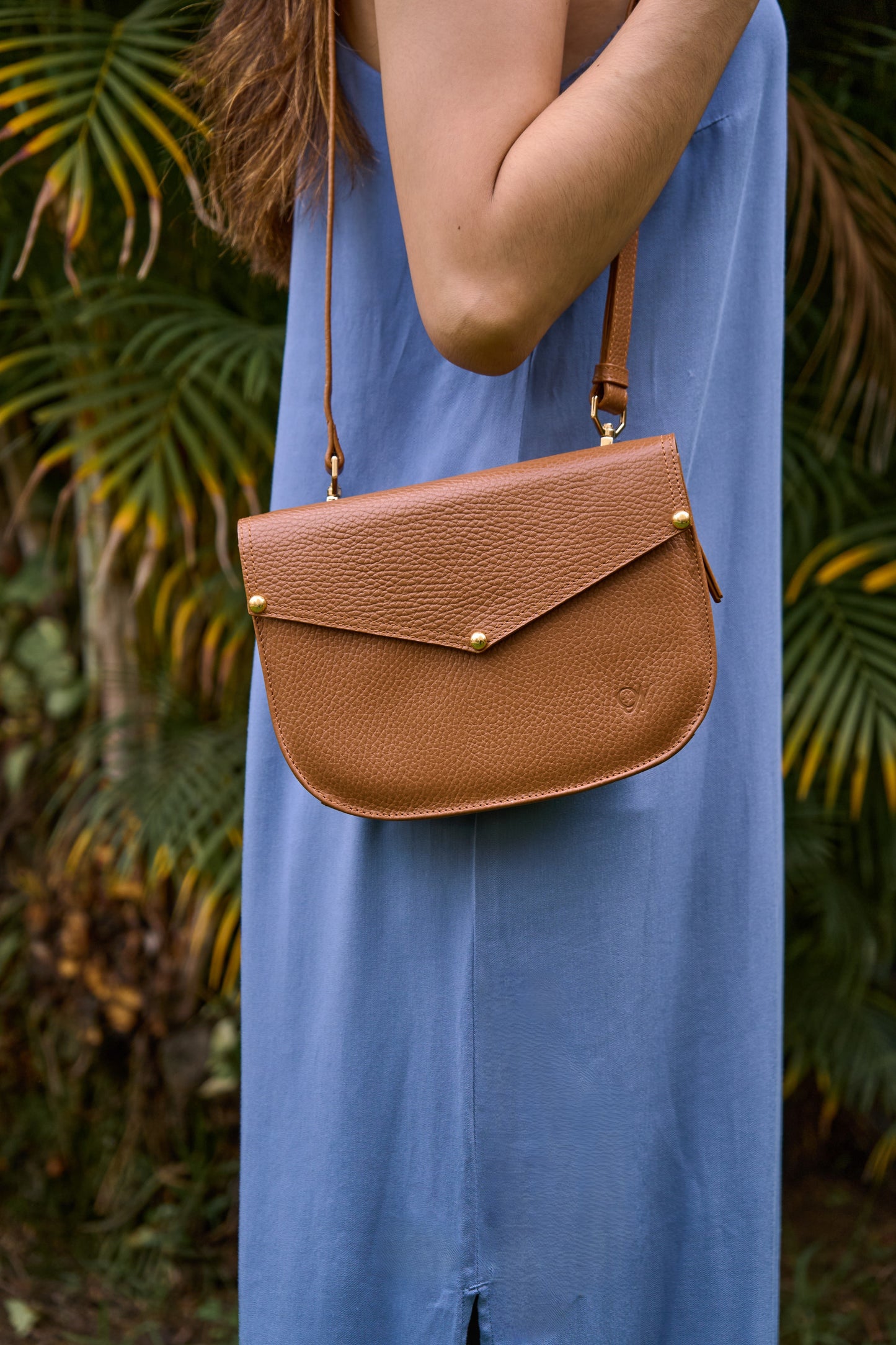 Model wearing a brown leather bag with a blue dress against a green leafy background