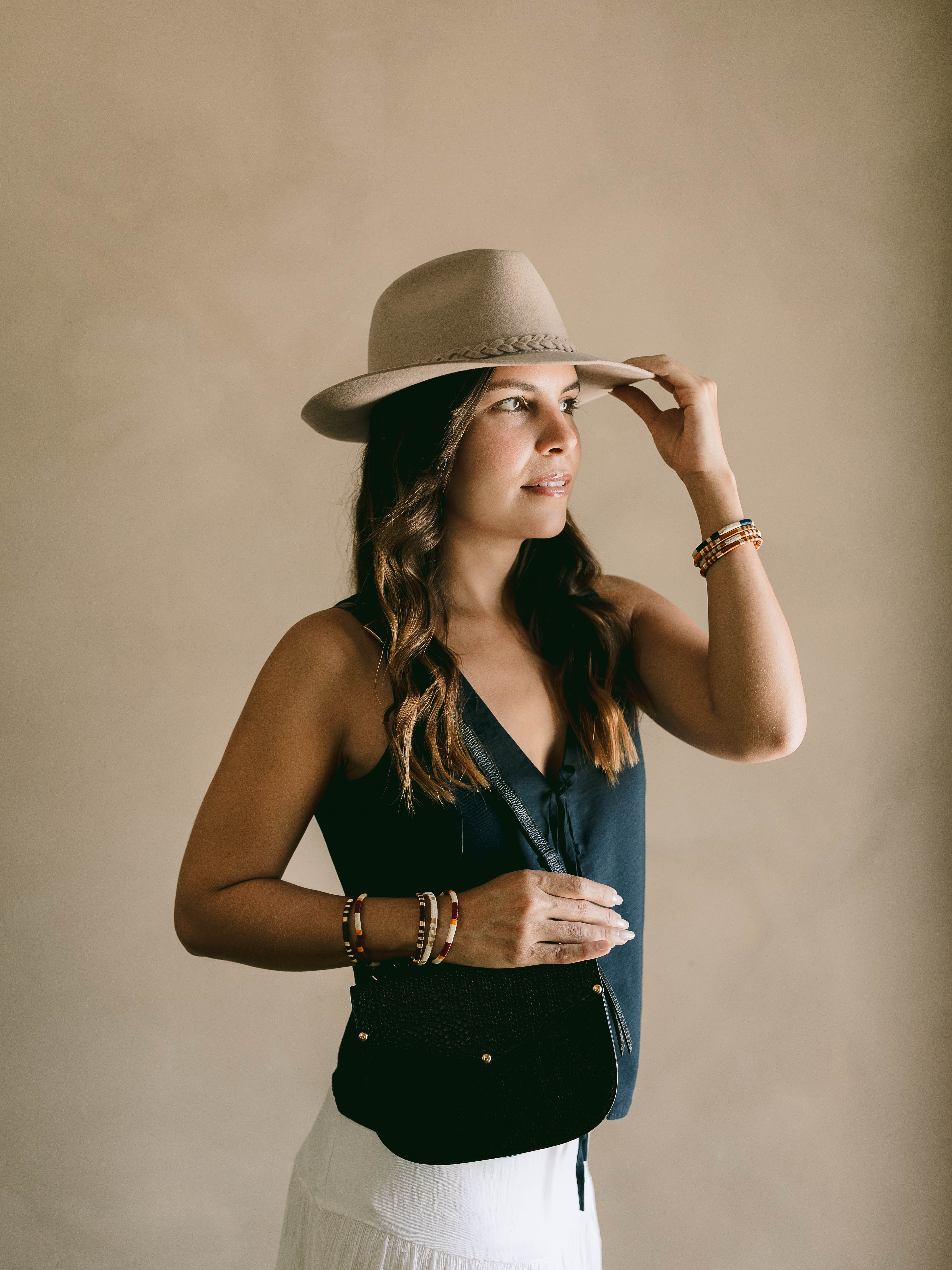 Woman wearing a beige hat and black top against a beige background