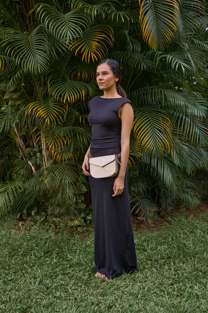 Woman in a dark dress standing in front of green foliage with bag across the waist